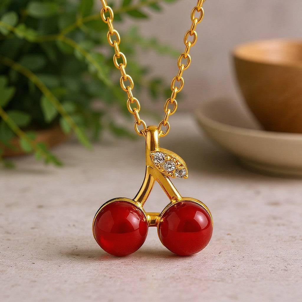 The Velvet Grove cherry pendant necklace featuring two glossy red beads and crystal-accented gold-tone stem on a chain