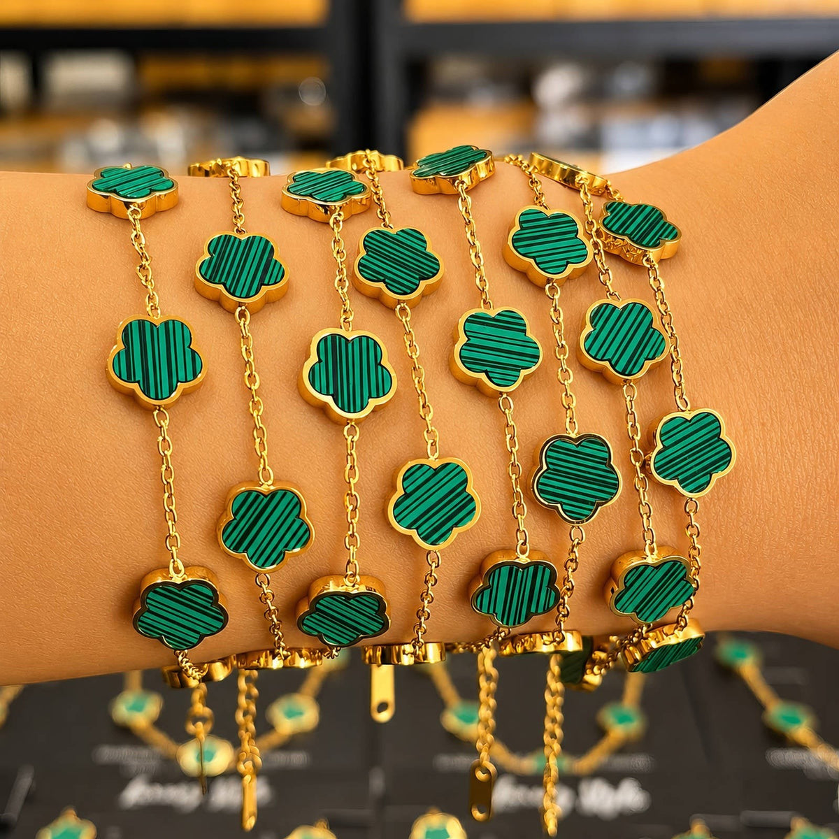 The Velvet Grove gold-tone link bracelet featuring emerald green striped clover-inspired floral motifs on a wrist.