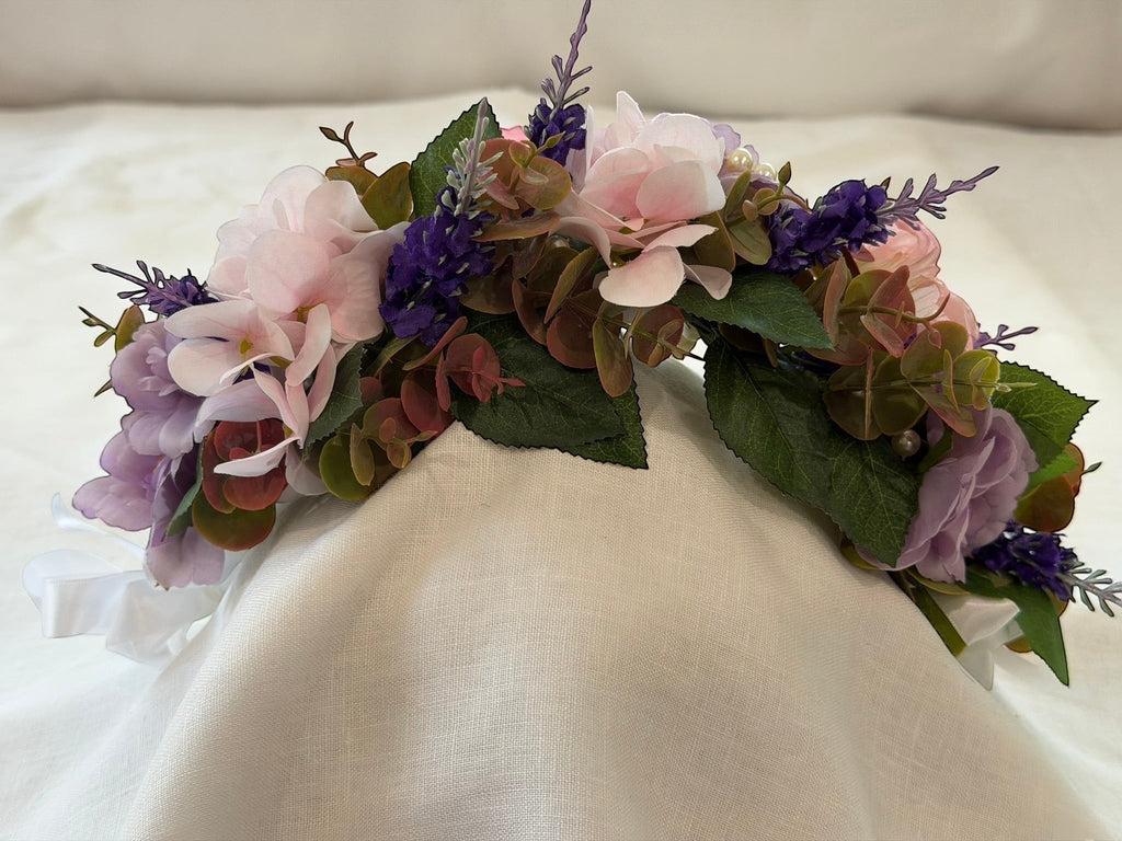The Velvet Grove floral crown with pink and purple faux flowers, green foliage, and pearls on a white fabric base.