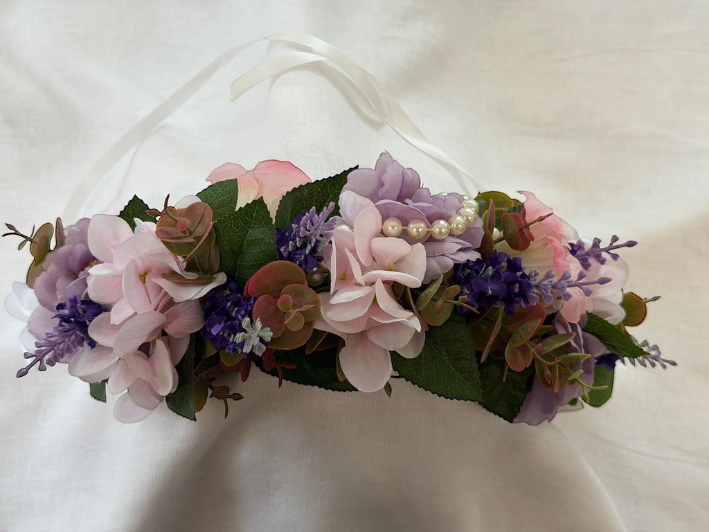 The Velvet Grove floral crown with pink and purple faux flowers, green foliage, and pearls with white ribbon ties.