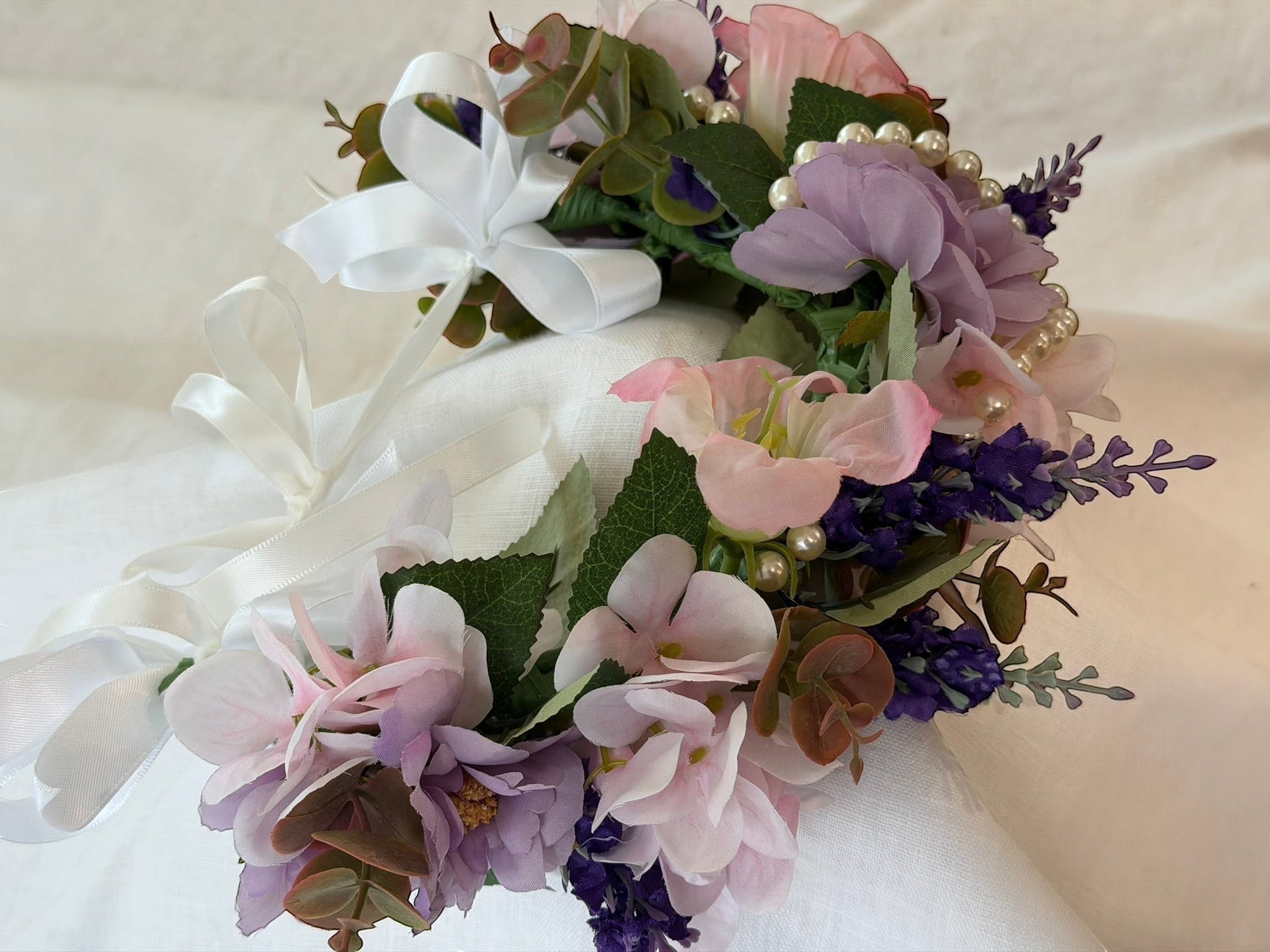 The Velvet Grove floral crown with pink and purple faux flowers, green foliage, and pearls with white ribbon ties.