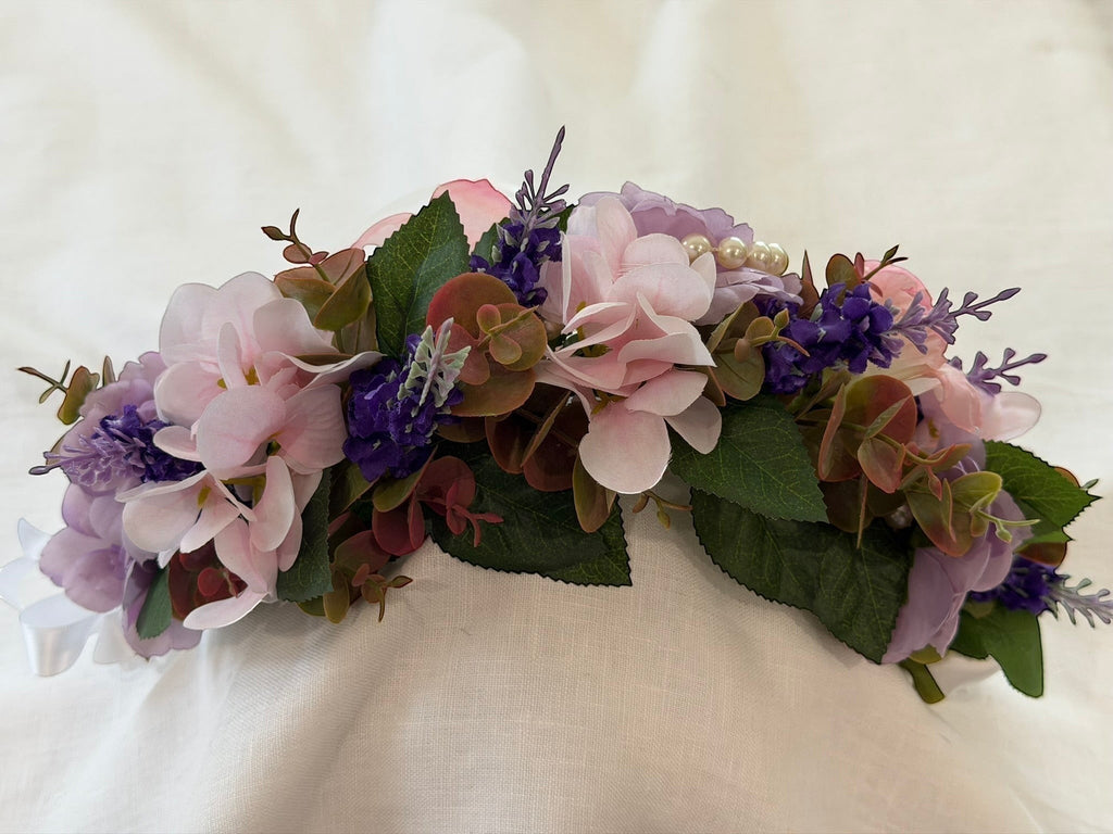 The Velvet Grove floral crown with pink and purple faux flowers, green foliage, and pearl accents on a white background