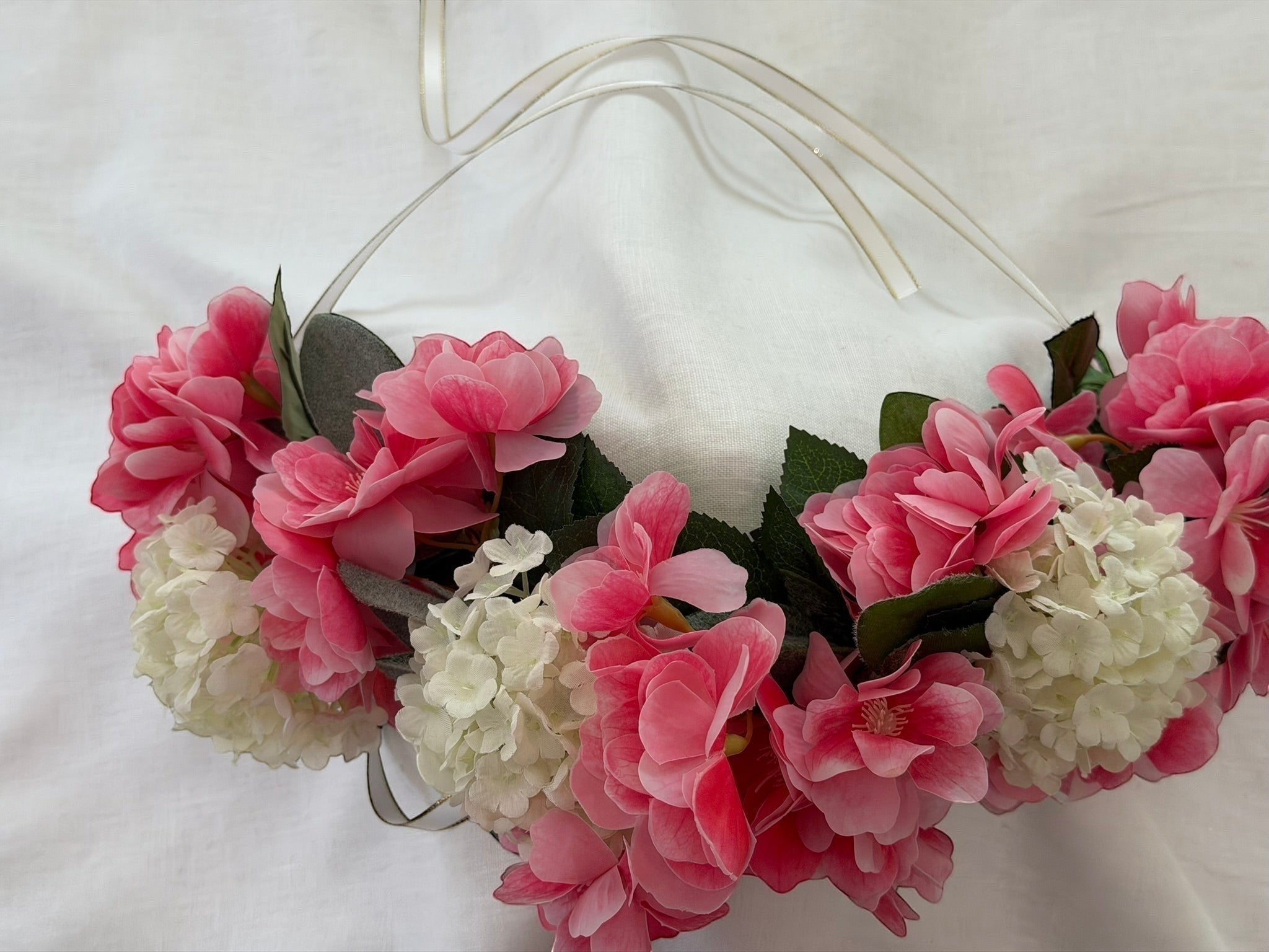 The Velvet Grove floral crown featuring vibrant pink blossoms, cream hydrangeas, and green foliage with ribbon ties.