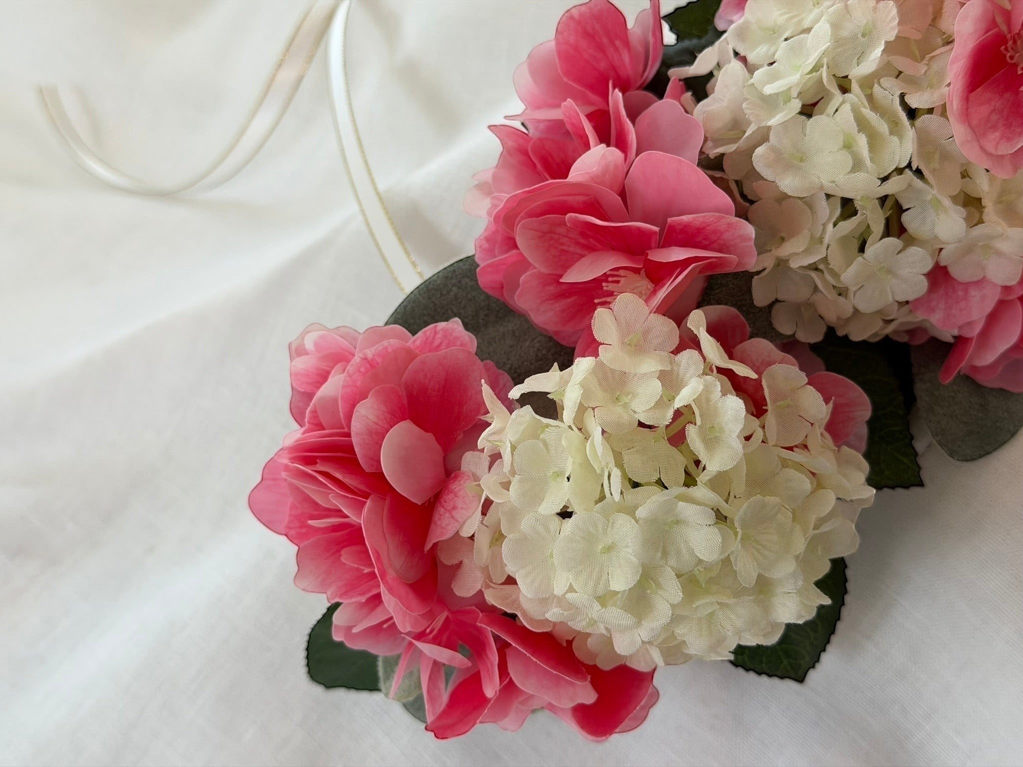 The Velvet Grove floral crown featuring vibrant pink blossoms and cream hydrangeas with green foliage and ribbon ties.