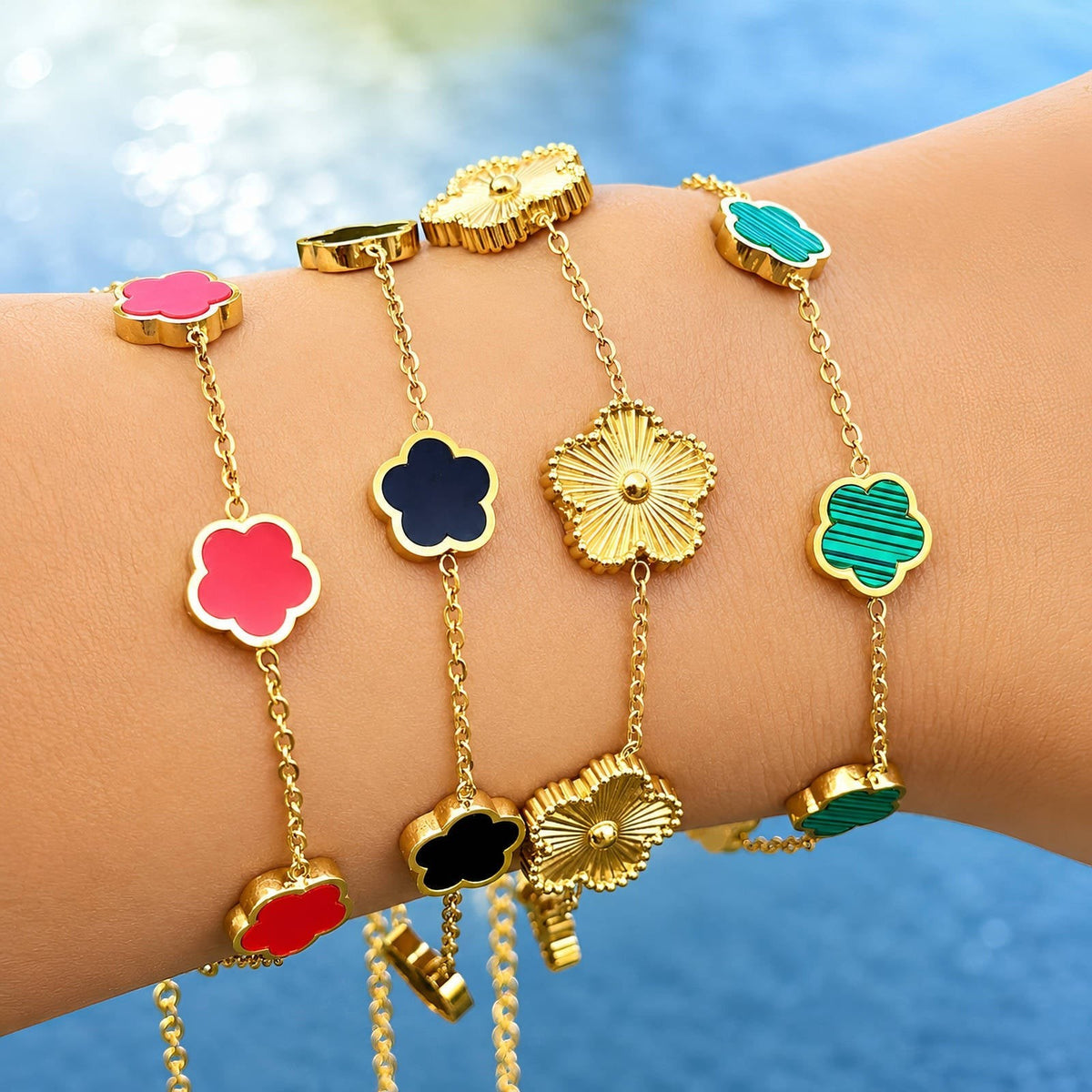 The Velvet Grove gold-tone chain bracelets featuring colorful flower motifs in red, black, and green on a wrist.