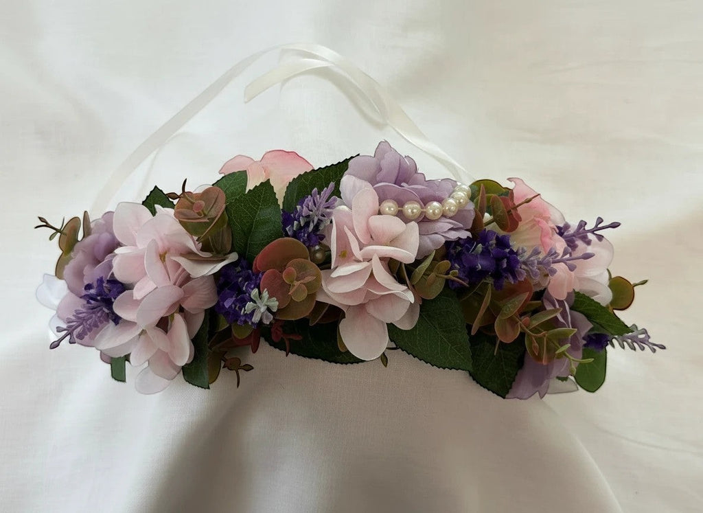 The Velvet Grove floral crown with pink and purple faux flowers, green foliage, and pearl accents on white ribbon ties.