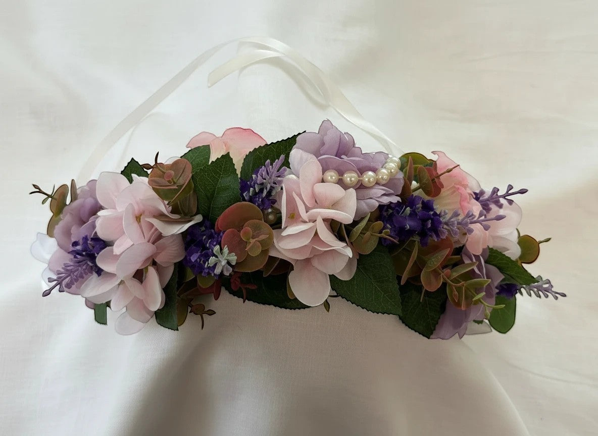 The Velvet Grove floral crown with pink and purple faux flowers, green foliage, and pearl accents on white ribbon ties.