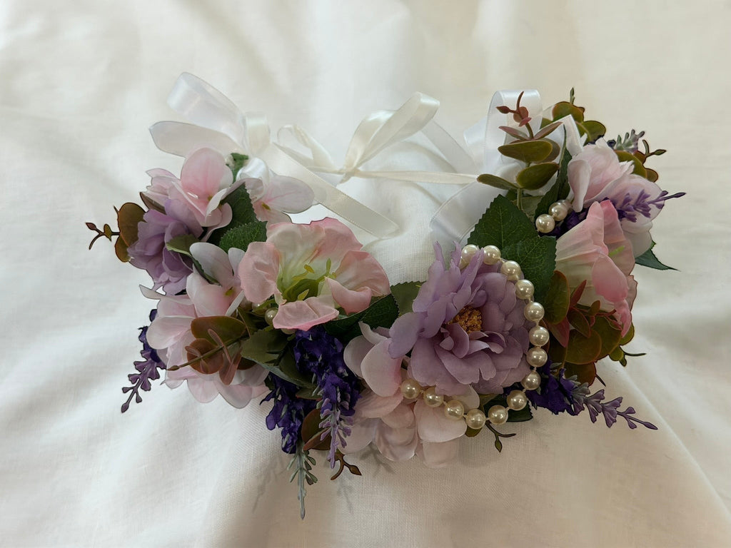 The Velvet Grove floral crown with pink and purple faux flowers, green foliage, and pearl accents with white ribbon ties.