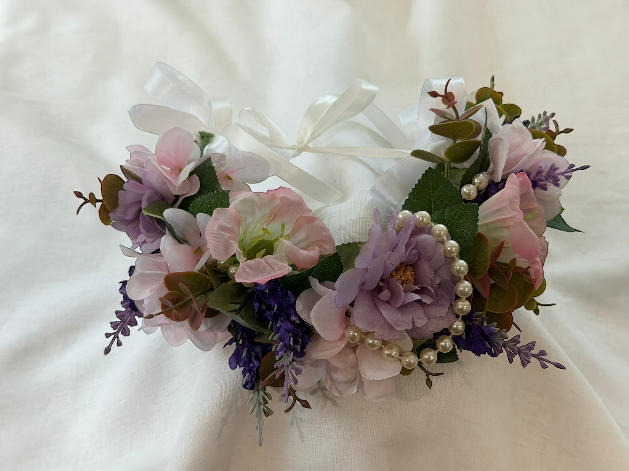 The Velvet Grove floral crown with pink and purple faux flowers, green foliage, and pearl accents with white ribbon ties.