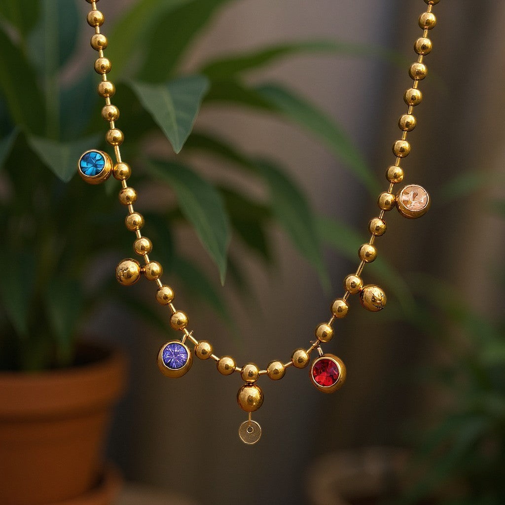 The Velvet Grove gold-tone ball chain necklace featuring bezel-set multi-colored crystals in a blurred plant setting.