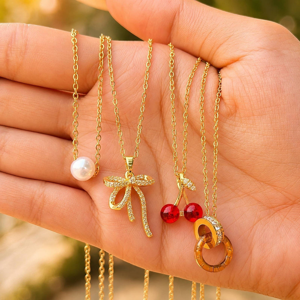 The Velvet Grove gold-tone necklaces featuring a cubic zirconia bow, a pearl, cherry charms, and a ring pendant.
