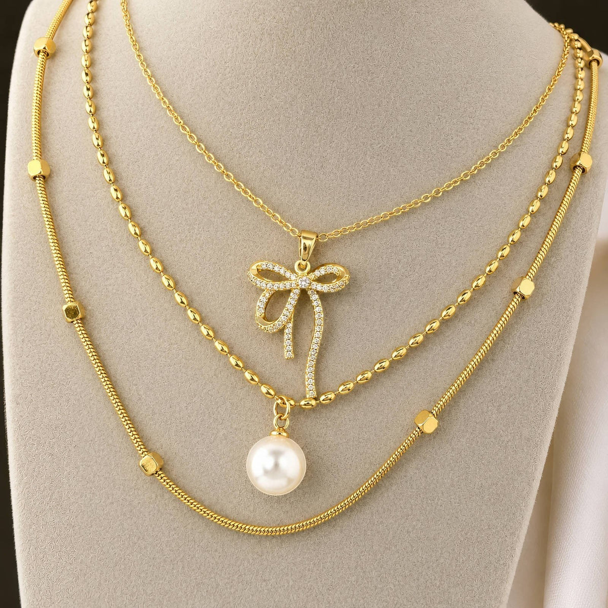 The Velvet Grove gold-tone layered necklace featuring a cubic zirconia bow pendant and a dangling white pearl charm.