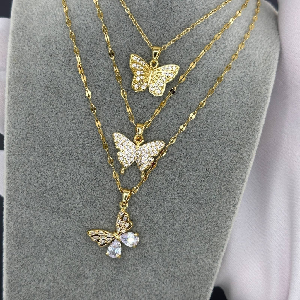The Velvet Grove gold butterfly pendant necklaces with sparkling crystals on a grey display stand.