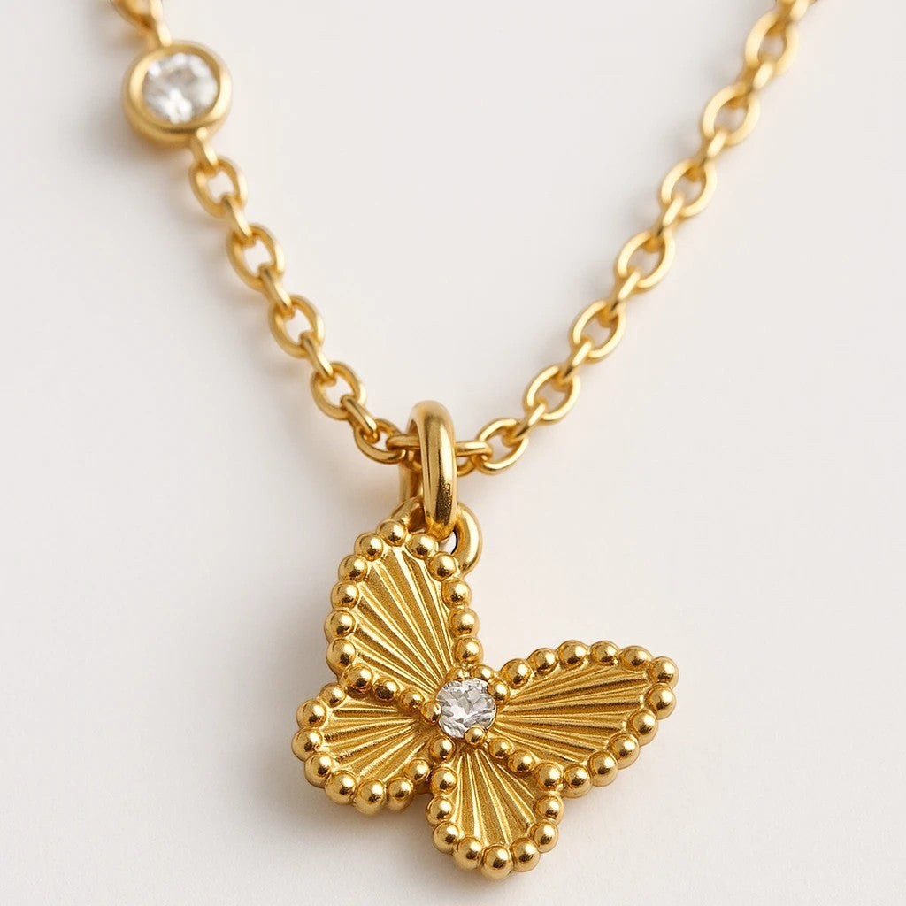 The Velvet Grove gold-tone butterfly pendant necklace with textured wings, beaded edges, and sparkling stone accents.