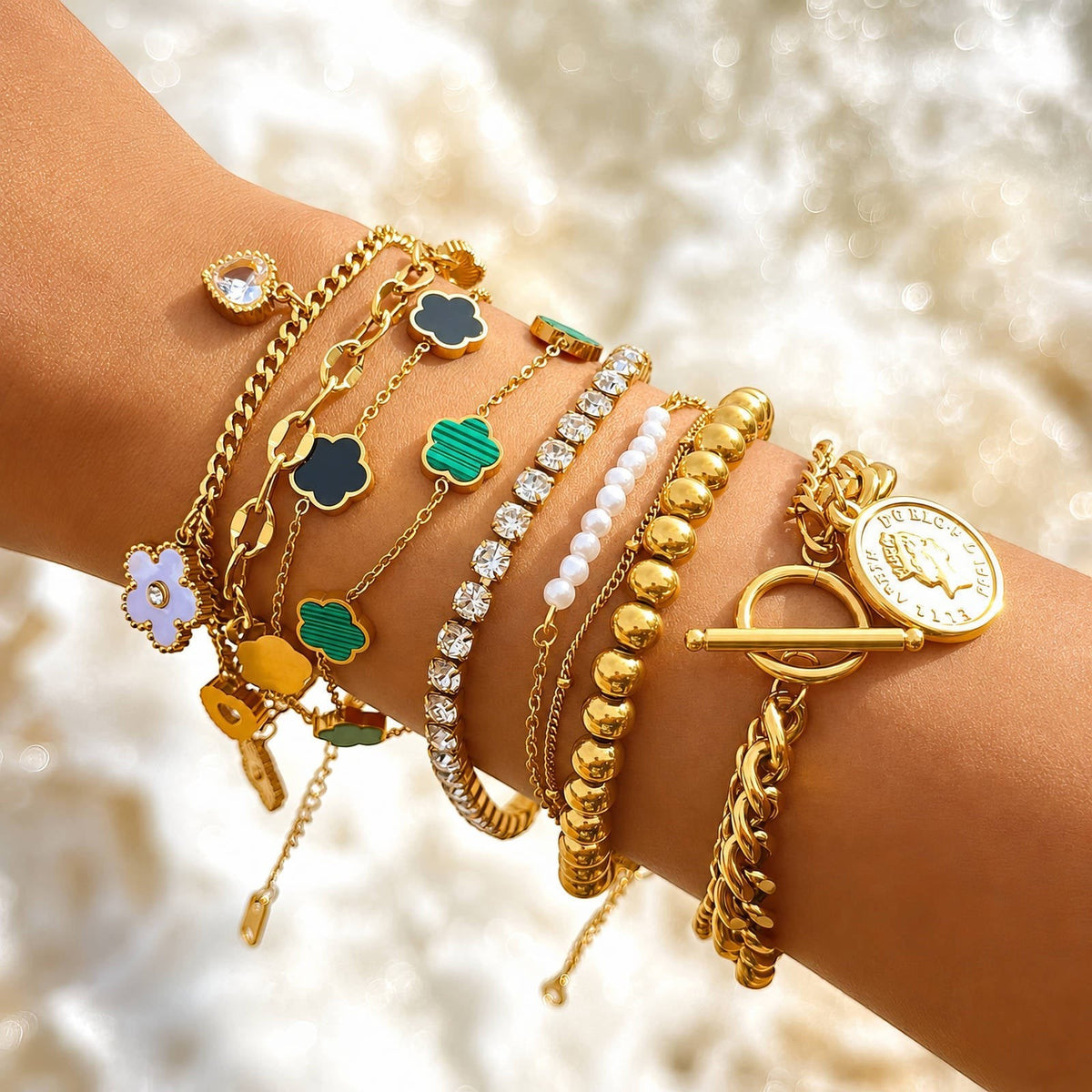 The Velvet Grove gold-tone bracelet stack featuring emerald green floral motifs, pearl accents, and a coin charm.