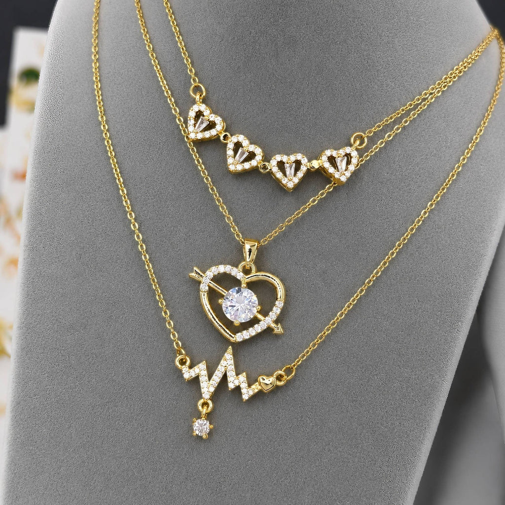 The Velvet Grove gold-tone layered necklace featuring heart, arrow, and heartbeat designs with sparkling crystals.