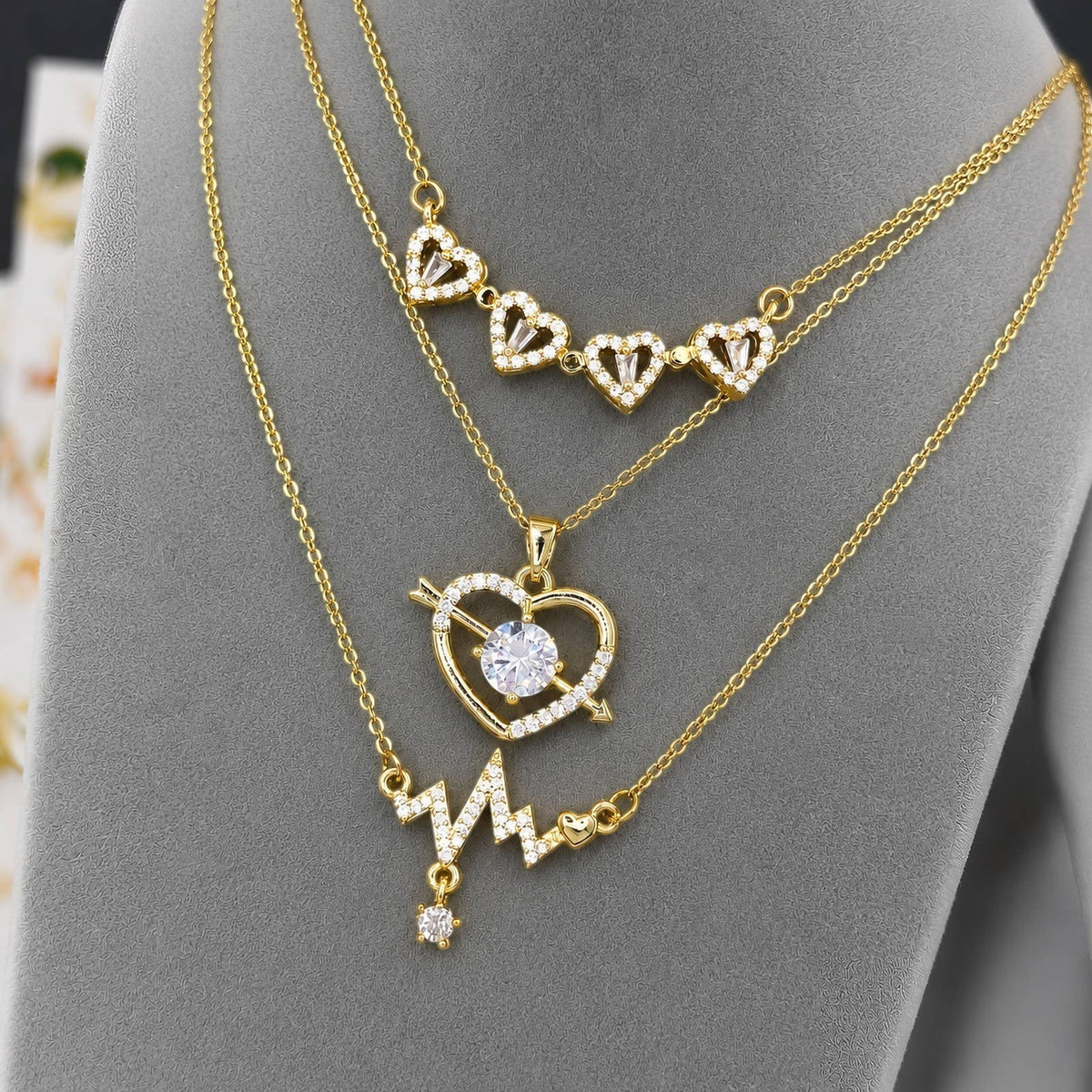 The Velvet Grove gold-tone layered necklace featuring heart, arrow, and heartbeat designs with sparkling crystals.