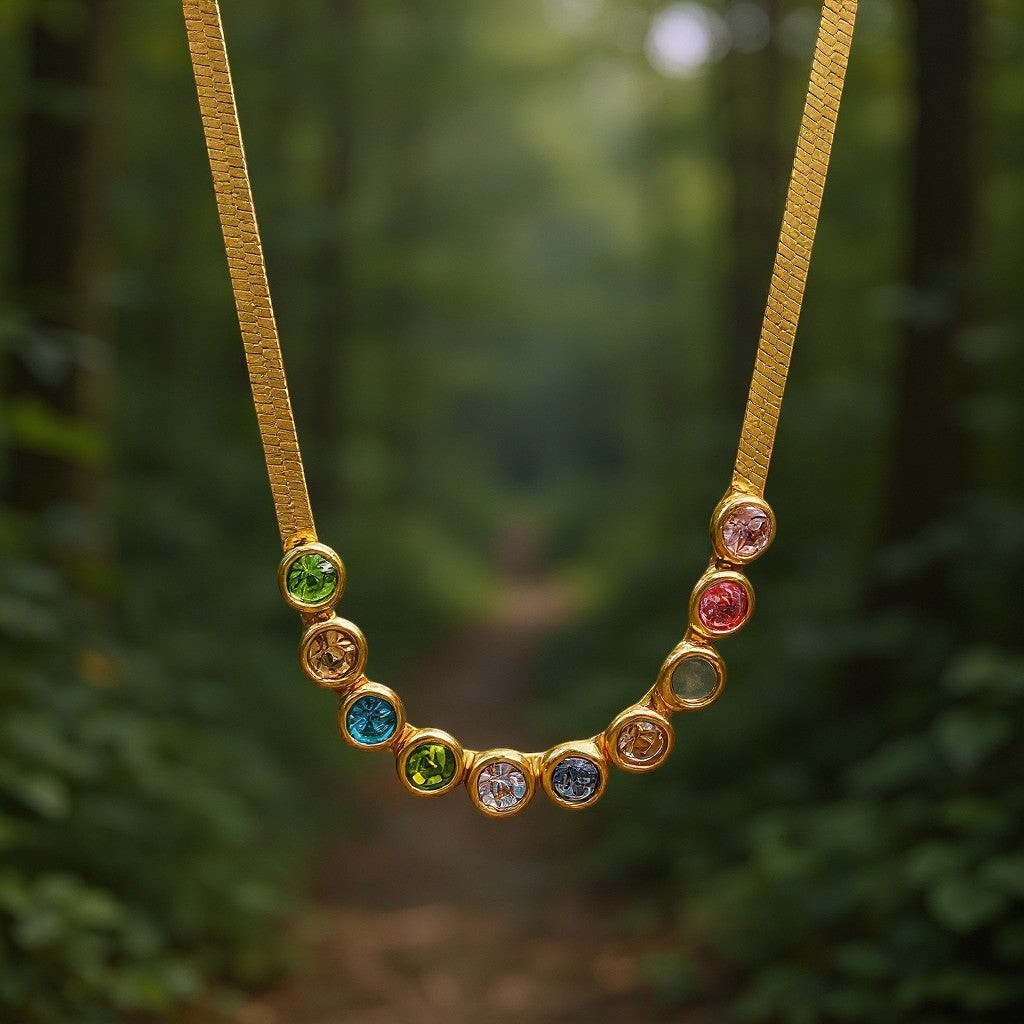 The Velvet Grove gold-tone herringbone chain necklace featuring a row of vibrant, bezel-set multi-colored stones.