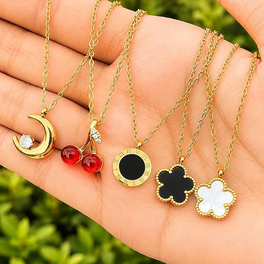 The Velvet Grove gold-tone necklaces featuring cherry, crescent moon, Roman numeral, and flower pendants on a hand.