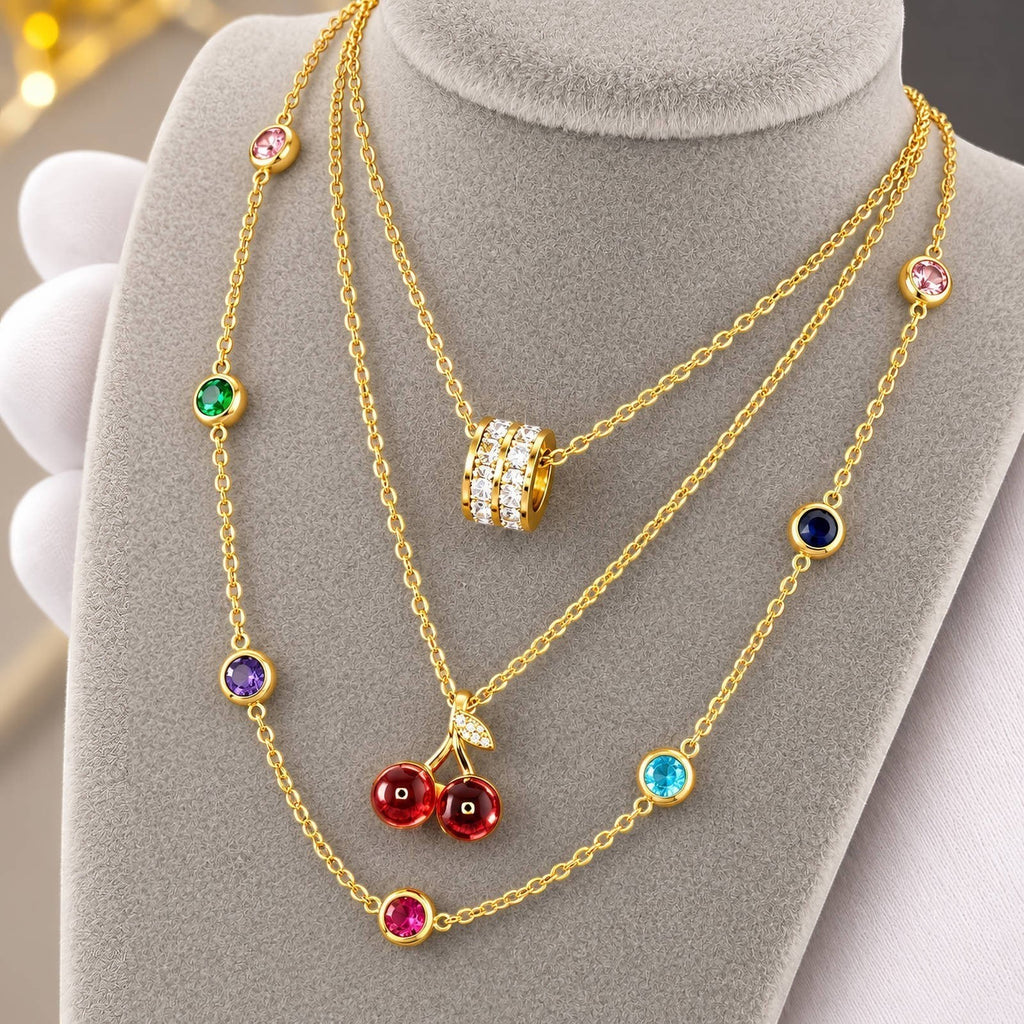 The Velvet Grove layered gold-tone necklace featuring a cherry pendant with red beads and crystal-accented multi-stones