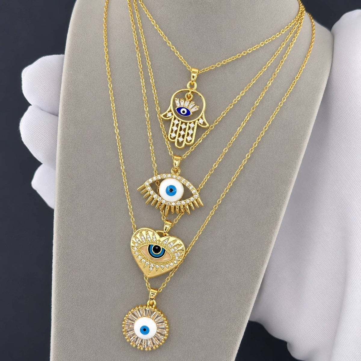 The Velvet Grove gold-tone layered necklace set featuring hamsa, evil eye, heart, and sunburst crystal pendants.