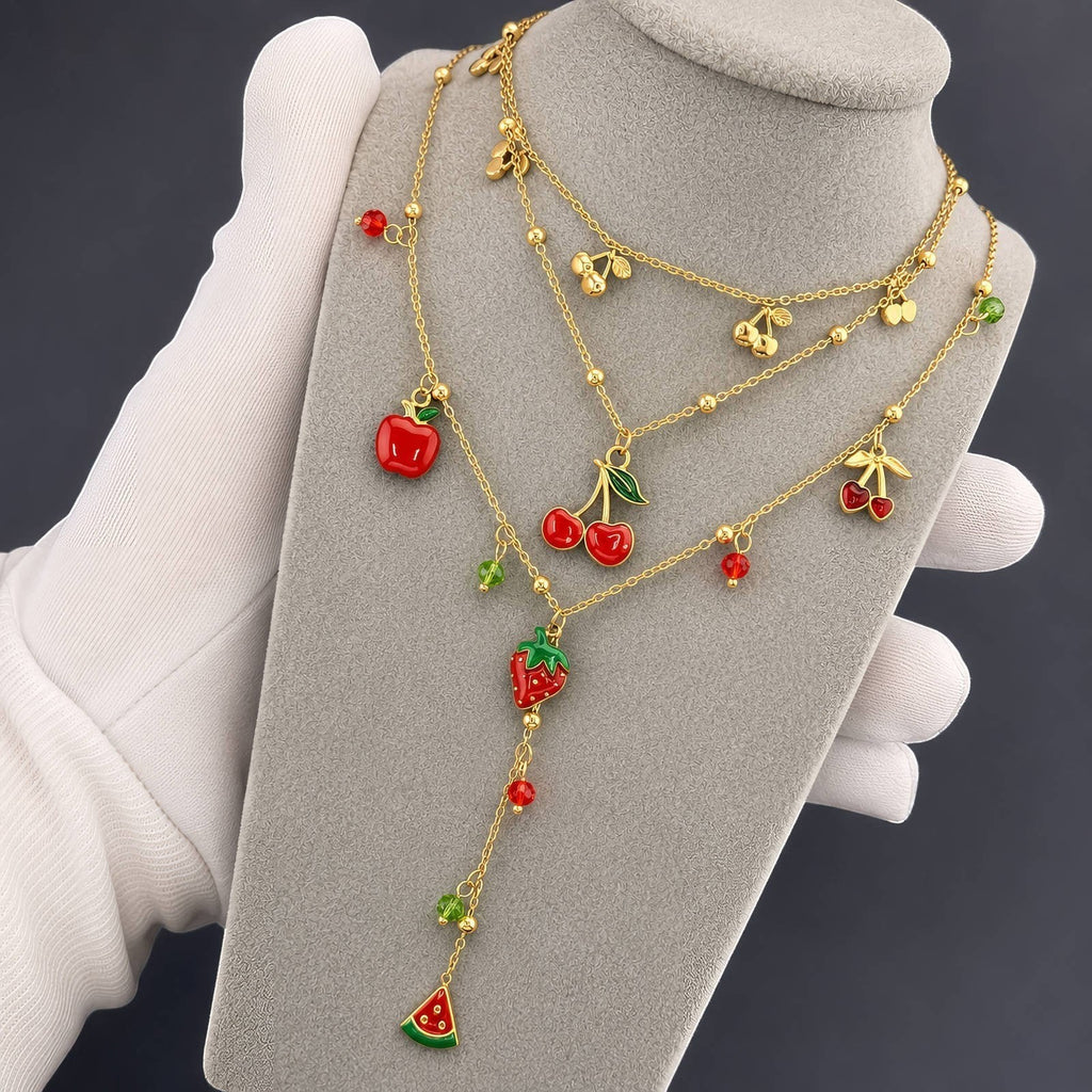 The Velvet Grove layered gold-tone necklace featuring vibrant enamel fruit charms like cherries, strawberries, and apple.