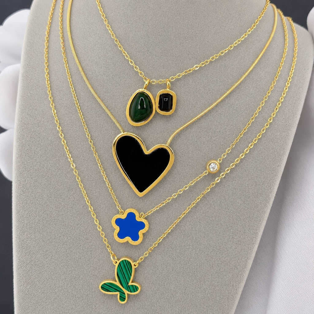 The Velvet Grove layered gold-tone necklaces featuring blue floral, black heart, green malachite, and crystal pendants.
