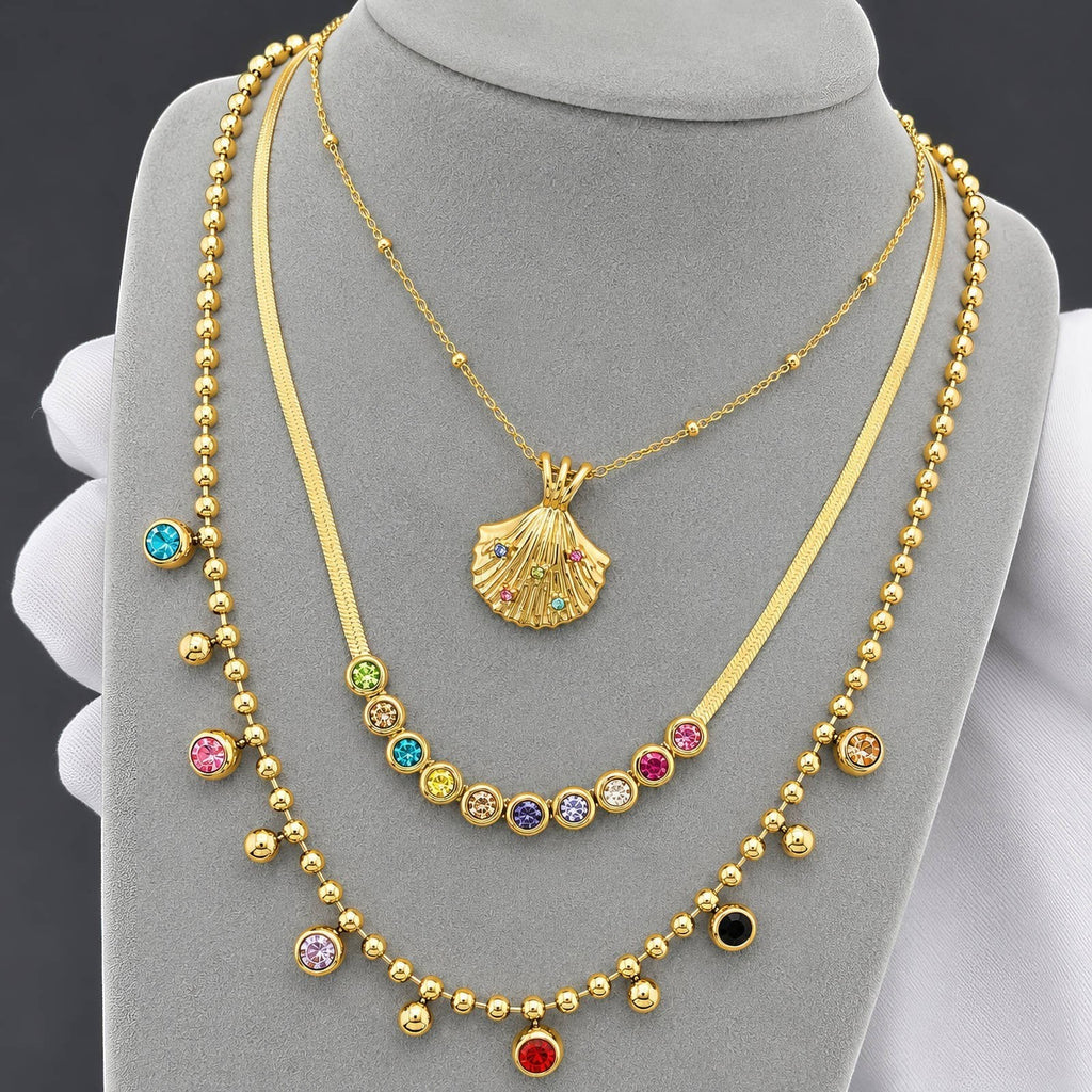 The Velvet Grove gold-tone layered necklace set featuring a herringbone chain, shell pendant, and multi-colored stones.