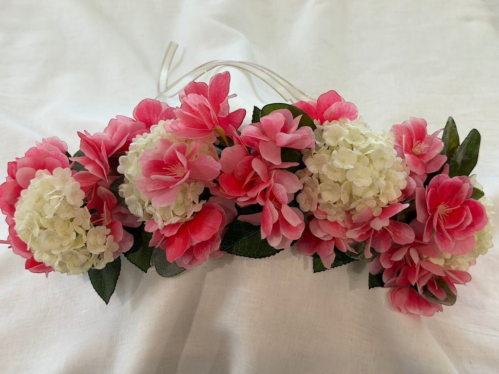 The Velvet Grove floral crown featuring vibrant pink blossoms, cream hydrangeas, and green leaves with ribbon ties.