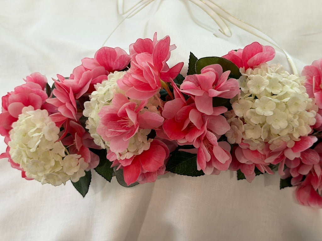 The Velvet Grove floral crown featuring vibrant pink blossoms, cream hydrangeas, and green foliage with ribbon ties.