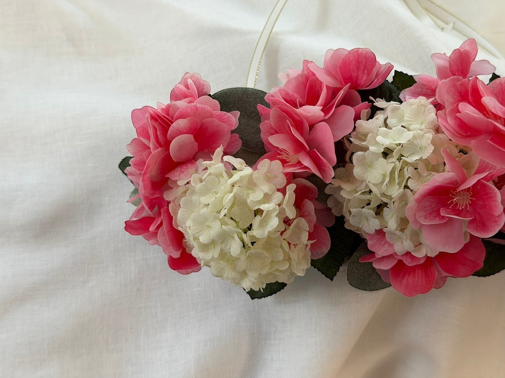 The Velvet Grove floral crown featuring vibrant pink blossoms and cream hydrangeas with green foliage on white fabric.