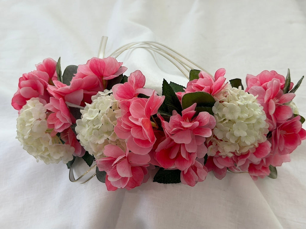 The Velvet Grove floral crown featuring vibrant pink blossoms, cream hydrangeas, and green foliage with ribbon ties.