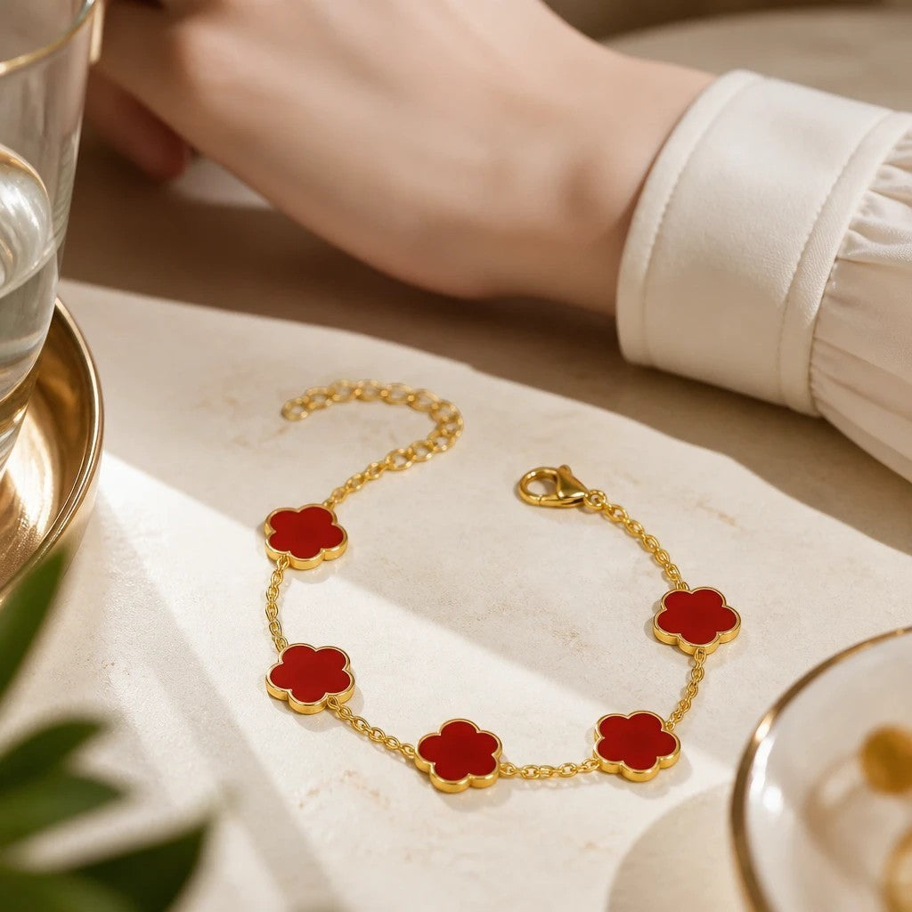 The Velvet Grove gold-tone link chain bracelet featuring vibrant red floral charms on a marble surface.