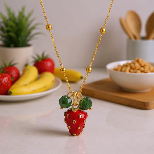 The Velvet Grove 18K gold plated stainless steel strawberry pendant necklace with green leaf accents on a gold chain.