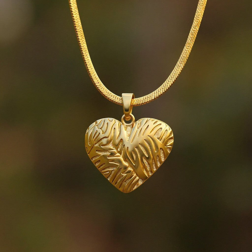 The Velvet Grove 18k gold plated steel necklace featuring a textured heart pendant on a sleek herringbone chain.