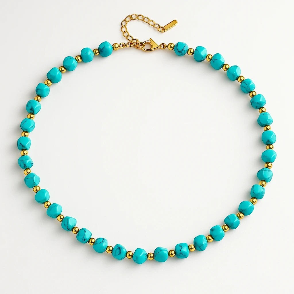 The Velvet Grove beaded statement necklace with turquoise-hued stones and polished gold-tone spacers on a white background